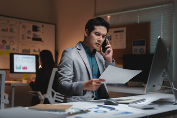 Young businessman talking on phone reviewing financial documents late