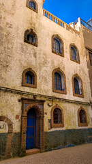 Fototapeta premium Essaouira Medina Charm: Historic Building Facade with Arched Blue Windows and Ornate Stone Entrance