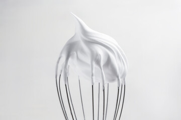 Whisk with whipped egg whites on light background, closeup