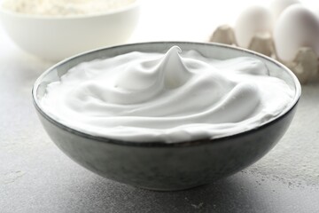 Beating egg whites in bowl on grey textured table, closeup