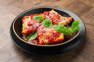 Delicious ravioli with tomato sauce, cheese and basil on wooden table, closeup