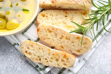 Fresh cut ciabatta, oil, olives and rosemary on grey textured table, top view