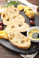 Pieces of fresh ciabatta, oil, olives, cheese and peppercorns on wooden table, closeup