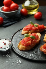 Tasty bruschettas with tomatoes and basil served on black table, closeup