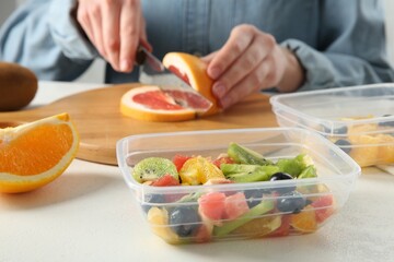 Making fruit salad. Woman cutting grapefruit at white table, closeup