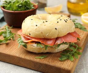 Delicious bagel with salmon and arugula on grey table, closeup