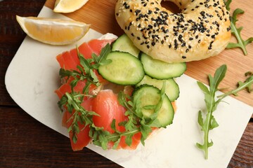 Delicious bagel with salmon, cucumber, arugula and lemon on wooden table, top view