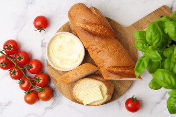 Cut baguette with butter, basil and tomatoes on white marble table, flat lay