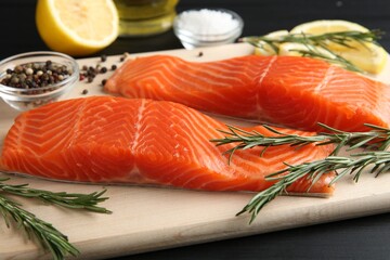Pieces of salmon fillet, spices and lemon on black wooden table, closeup