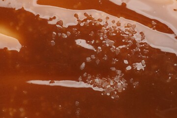 Delicious caramel sauce with salt as background, top view