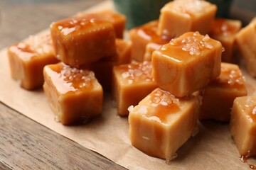 Tasty candies with salt and caramel sauce on wooden table, closeup