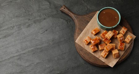 Tasty candies with salt and caramel sauce on dark textured table, top view. Space for text