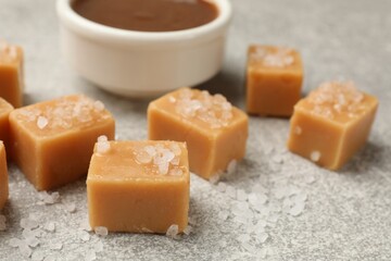 Tasty candies with salt and caramel sauce on grey textured table, closeup