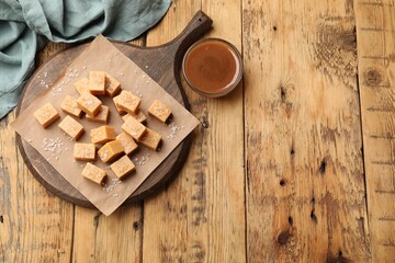 Tasty candies with salt and caramel sauce on wooden table, flat lay. Space for text