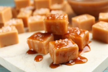Tasty candies with salt and caramel sauce on light blue table, closeup