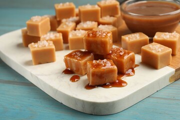 Tasty candies with salt and caramel sauce on light blue wooden table, closeup