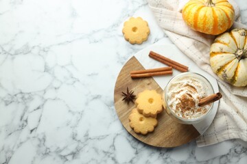 Tasty pumpkin latte with whipped cream in glass, cookies and ingredients on white marble table, flat lay. Space for text