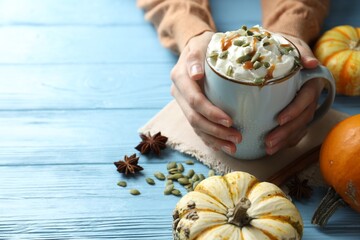 Woman holding tasty pumpkin latte with whipped cream at light blue wooden table, closeup. Space for...
