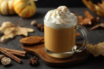 Tasty pumpkin latte with whipped cream in glass cup, spices and autumn decor on grey table, closeup