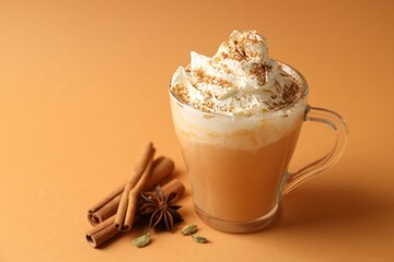Tasty pumpkin latte with whipped cream and spices on orange background, closeup. Space for text