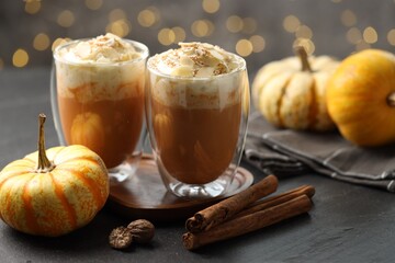 Tasty pumpkin latte with whipped cream, spices and fresh vegetables on black table against blurred...