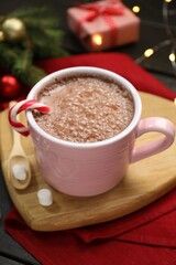 Tasty hot cocoa drink with candy cane in cup marshmallows and Christmas decor on dark wooden table