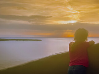 Fototapeta premium Silhouetted figure of a child against the colorful golden-hour sky in the picturesque cliffside village of Santorini.