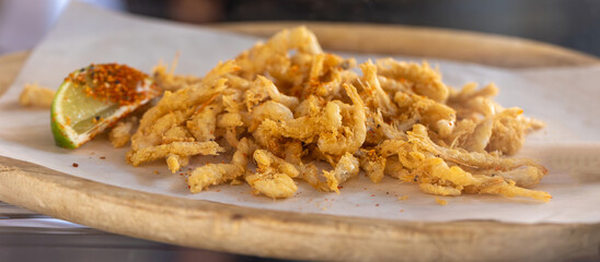 Battered and fried small shrimp piled on parchment paper, seasoned with spices and a lime