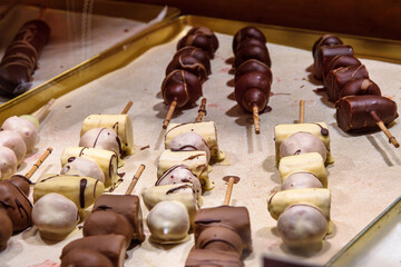 Closeup of a chocolate coated fruit skewers. Rows of chocolate dipped apple, banana strawberry skewers lined up at a Christmas market stall. Schokofrucht - Traditional German holiday treat 
