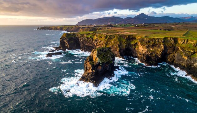 Rocky coastline with cliffs and mountain backdrop under cloudy sky, ocean waves crashing - Powered by Adobe