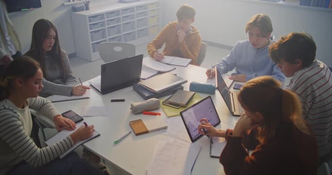 Concentrated Students Collaborate Around Shared Table, Combining Digital Tools and Handwritten Notes. Concept of Teamwork, Creative Problem Solving, and Blended Learning in Modern Classroom Setting.