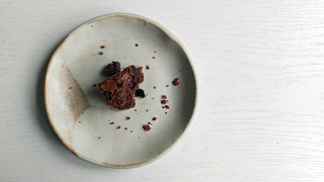 Remains of some chocolate chip cookies on small plate. Handmade rustic ceramic saucer with crumbs set against light wooden background. Breakfast is over on wooden table