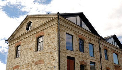 Historic stone building facade, renovated. Traditional arched windows, light brick, modern black dormers and sleek roof. Urban architectural blend. Real estate, urban living, and property marketing.