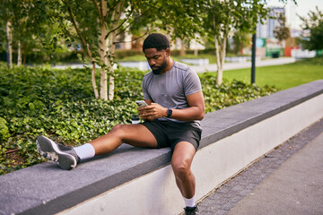 Athlete Checks Phone After Run At Park Bench With Hydration Bottle Nearby And Focused Mood