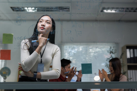 Asian businesswoman brainstorming ideas on glass board