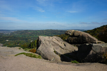 Panoramic View Of Ancient Gritstone Rock Formations At Black Rocks, Cromford, Derbyshire, Overlooking A Vast Autumn Landscape And Distant Town Under A Clear Blue Sky.