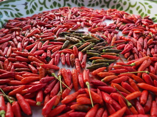 A vibrant close-up food photograph capturing the natural maturation cycle of Bird's Eye Chilies. The composition highlights the color transition from deep green/brown to fiery red, symbolizing the dev