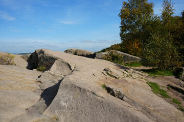Sunny View Of Large, Weathered Gritstone Rock Formations With Names Carved Into Them At Black Rocks, Cromford, Derbyshire, Under A Clear Blue Sky.