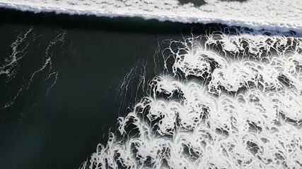 An mesmerizing aerial perspective captures the dynamic power and intricate beauty of ocean waves crashing and spreading. White foam forms stunning, ever-changing abstract patterns as it retreats acros