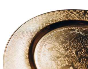 Close up of a golden ornate metal plate with intricate engraved patterns and a dark background casting soft light on the textured surface emphasizing metallic sheen and detailed craftsmanship