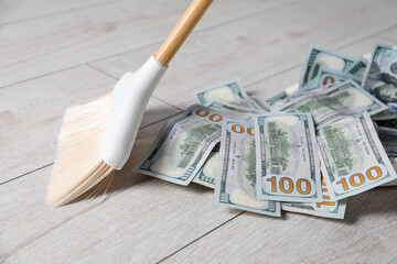 Sweeping dollar banknotes with broom on light wooden floor, closeup