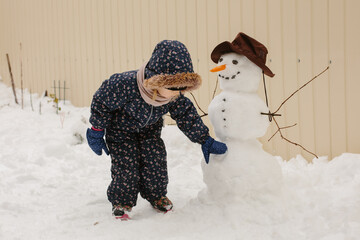 Little child playing with snowman in snowy yard