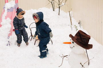Children playing with snowman in winter backyard snow
