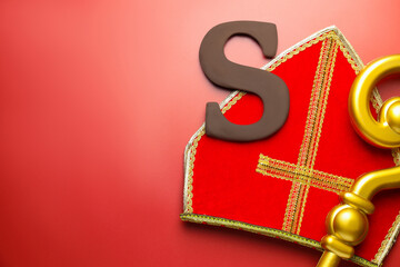 Saint Nicholas (Sinterklaas) day. Mitre, crosier and chocolate letter S on red background, flat...