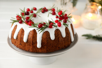 Tasty Christmas cake with icing, cranberries and rosemary on white wooden table, closeup