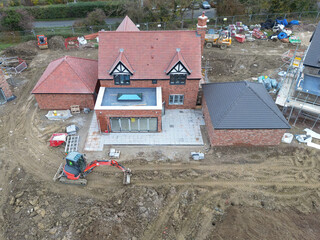 Drone inspection view of a large, near completed family home seen with a newly fitted glass lantern on the conservatory roof. Seen at a British housing development site.