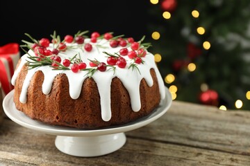 Delicious Christmas cake with icing, cranberries and rosemary on wooden table against black background with blurred lights, closeup with space for text. Bokeh effect