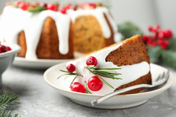 Piece of delicious Christmas cake with icing, cranberries and rosemary on grey textured table, closeup