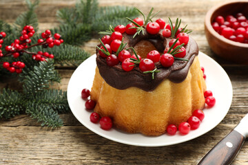Delicious Christmas cake with chocolate glaze, cranberries, rosemary and fir tree branches on wooden table, closeup