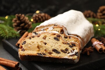 Traditional Christmas Stollen with icing sugar, spices and festive decor on black table, closeup
